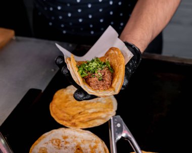 Guadalajara stili birria taco hazırlayan kişi tortilla, soğan ve kişniş.