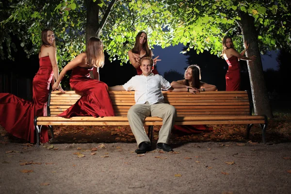 Man on bench, surrounded by sexy woman — Stock Photo, Image