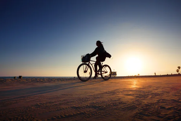 Biker silhouet rijdend langs het strand bij zonsondergang — Stockfoto