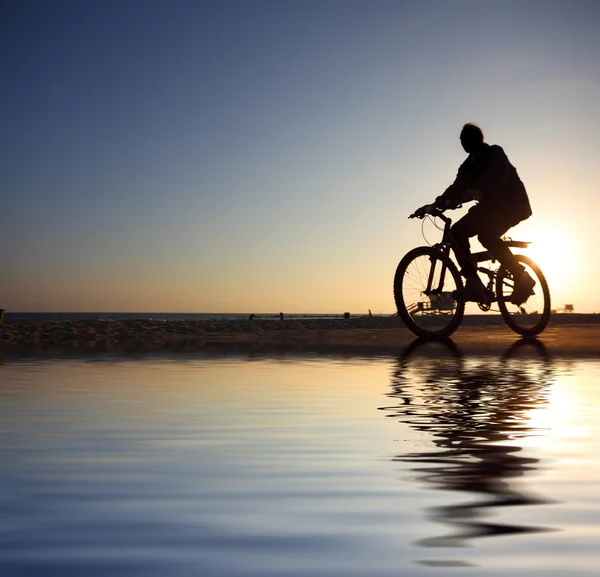 Biker silhuett ridning längs stranden vid solnedgången — Stockfoto