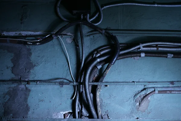 Old pipes and wires running along dark wall — Stock Photo, Image