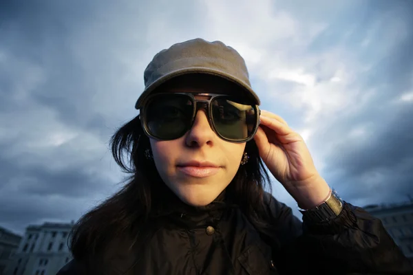 Wide angle portrait of brunette girl in sunglasses over cloudy sky — Stock Photo, Image