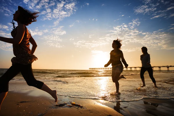 Three girls running by the ocean at sunset — Stock Photo, Image