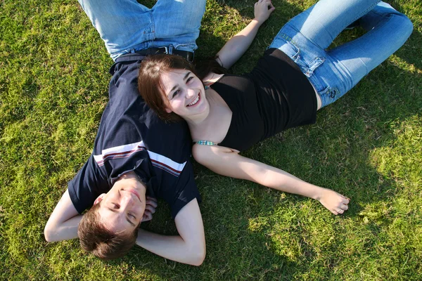 Happy young couple lying on green field — Stock Photo, Image