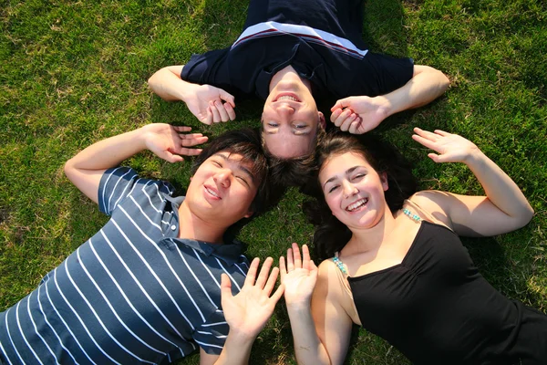 Three happy friends lying on green grass — Stock Photo, Image