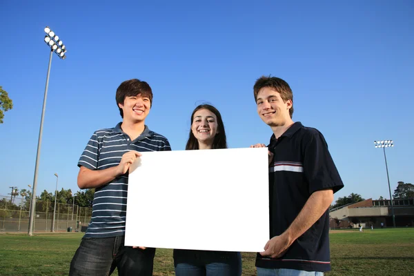 Three young friends holding a blank white billboard — Stock Photo, Image