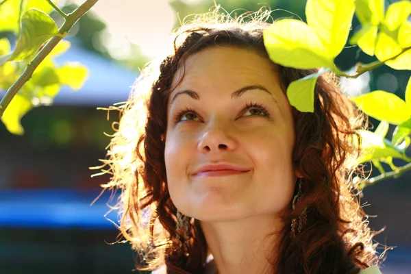 Sorrindo jovem mulher sob folhas verdes . Fotos De Bancos De Imagens