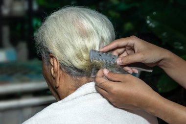 Evde yaşlı annesinin saçını kesen bir kadının eli.