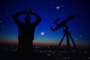 Astronomi teleskopu ve dürbünle yıldızlı gökyüzünü izleyen bir adamın silueti..