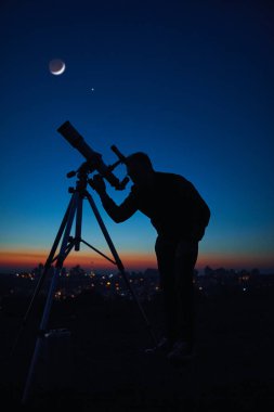 Yıldızlı gökyüzünün altında bir adamın silueti ve teleskop..