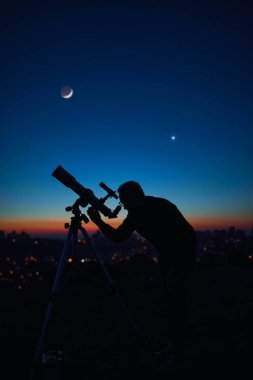 Yıldızlı gökyüzünün altında bir adamın silueti ve teleskop..