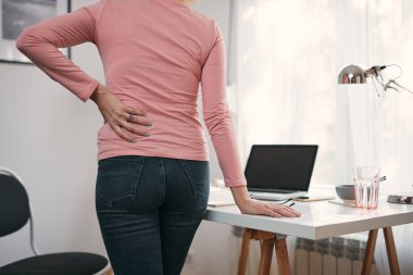 Kalçası, sırtı, omurga spazmı, kramp ve ağrısı olan, ev sorunları ve sorunları ile çalışan bir kadın..