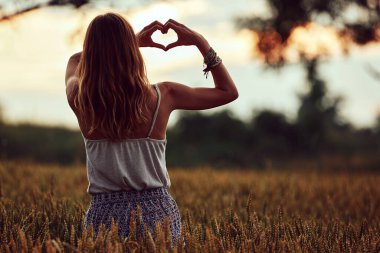 Doğadaki kadın ellerle yapılmış kalp şeklinde bir sembol tutuyor..