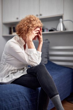 Baş ağrısı, akşamdan kalma, zihinsel ve depresyon sorunları olan bir kadın evde bir yatakta oturuyor..