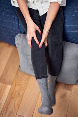 Kasılma, kramp, burkulma, çıkık diz ve eklem ağrısı olan bir kadın evde egzersiz yapıyor..