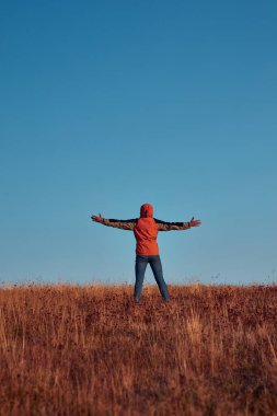 Kolları açık bir adam dağın tepesinde eğleniyor..
