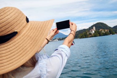 Genç, yetişkin bir turist kadın modern bir akıllı telefonla fotoğraf çekerken gölde eğleniyor..
