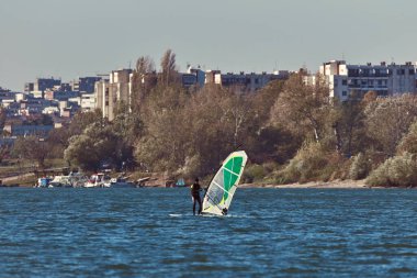 Rüzgâr sörfçüsü şehir nehrinde rüzgarlı bir günde sörf yapıyor..