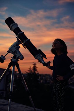Astronomik teleskopu olan bir kız alacakaranlık gökyüzü altında yıldızlara bakıyor..