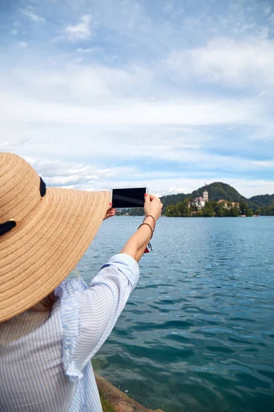 Genç, yetişkin bir turist kadın modern bir akıllı telefonla fotoğraf çekerken gölde eğleniyor..