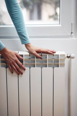 Soğuk kış günlerinde ellerini radyatörde ısıtan kadın..