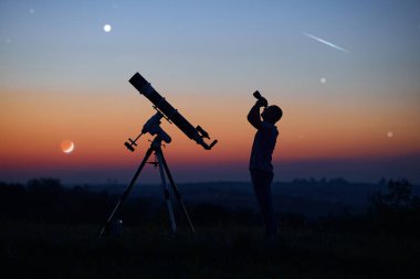 Bir adamın silueti, teleskop ve kırsal alan yıldızlı gökyüzünün altında.