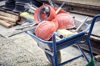 Several protective construction helmets and tools in wheelbarrow on a public road reconstruction.
