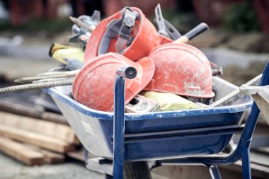 Several protective construction helmets and tools in wheelbarrow on a public road reconstruction.