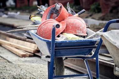 Several protective construction helmets and tools in wheelbarrow on a public road reconstruction.