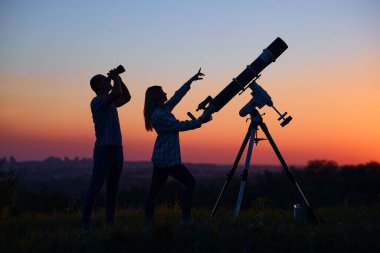 Couple stargazing together with a astronomical telescope. clipart