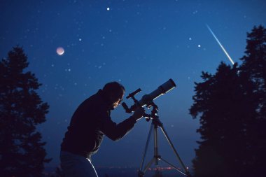 İnsan silueti, teleskop, yıldızlar, gezegenler ve gece gökyüzünün altında kayan yıldız..