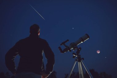 İnsan silueti, teleskop, yıldızlar, gezegenler ve gece gökyüzünün altında kayan yıldız..