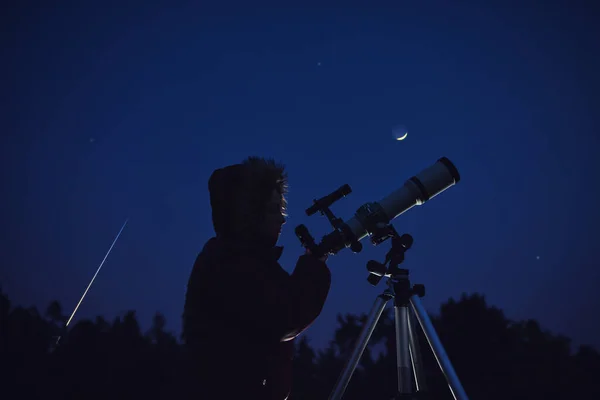 Silhouette of a woman, telescope, stars, planets and shooting star under the night sky.
