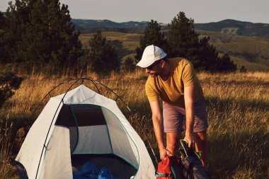 Doğada kamp yapan, küçük çadırları açan ve paketleyen, dinlenme ve hobileri olan bir adam..