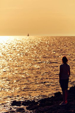 Uzak ufukta gün batımını izleyen bir kadının silueti..
