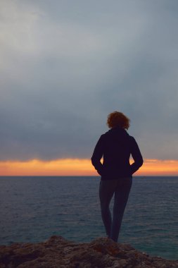 Uzak ufukta gün batımını izleyen bir kadının silueti..