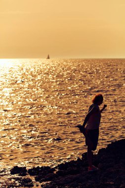 Okyanusun üzerinde günbatımının doğuşunu seyreden bir kadının silueti..