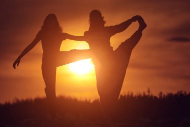 Anne ve kızı doğada gün batımında birlikte yoga yapıyorlar..