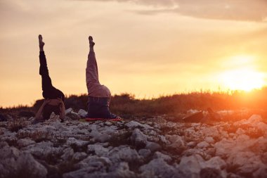 Anne ve kızı doğada gün batımında birlikte yoga yapıyorlar..