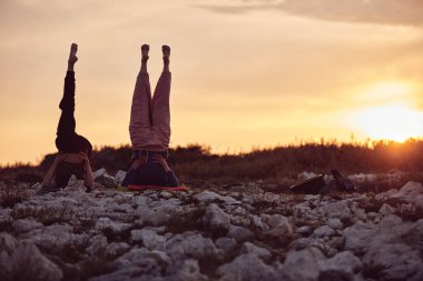 Anne ve kızı doğada gün batımında birlikte yoga yapıyorlar..