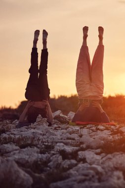 Anne ve kızı doğada gün batımında birlikte yoga yapıyorlar..