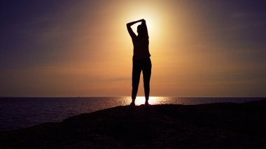 Okyanusun üzerinde günbatımının doğuşunu seyreden bir kadının silueti..