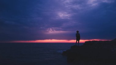 Uzak ufukta gün batımını izleyen bir kadının silueti..