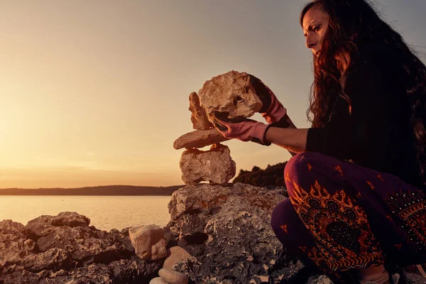 Silhouette of a woman balancing rocks and stones on the ocean sea coast at sunset sunrise time.