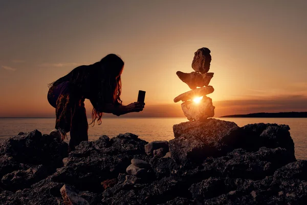 Silhouette of a woman balancing rocks and stones on the ocean sea coast at sunset sunrise time.