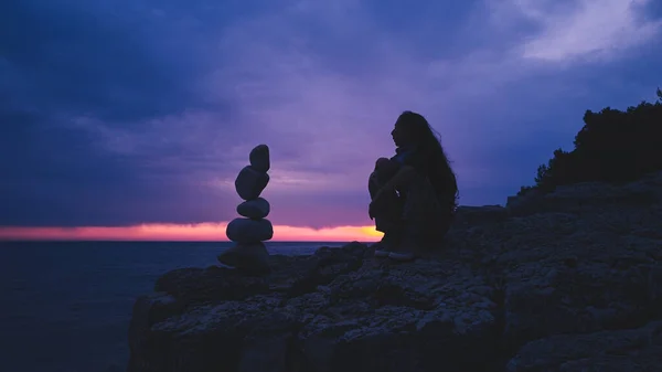 Silhouette of a woman balancing rocks and stones on the ocean sea coast at sunset sunrise time.