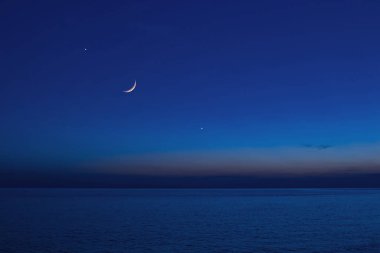 Yıldızlı gökyüzü ve okyanus ufkunun üzerinde gezegenleri olan bir ay..