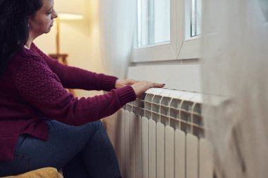 Soğuk bir kış gününde ısınan kadın, enerji ve gaz krizi, soğuk oda, ısıtma sorunları.