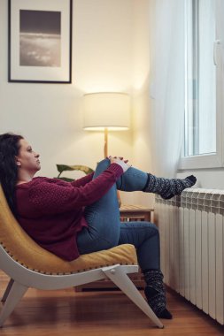 Soğuk bir kış gününde ayakları ısıtan kadın, enerji ve gaz krizi, soğuk oda, ısıtma sorunları.