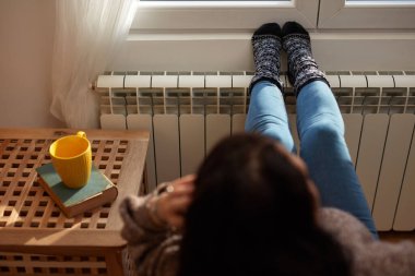 Soğuk bir kış gününde ayakları ısıtan kadın, enerji ve gaz krizi, soğuk oda, ısıtma sorunları.